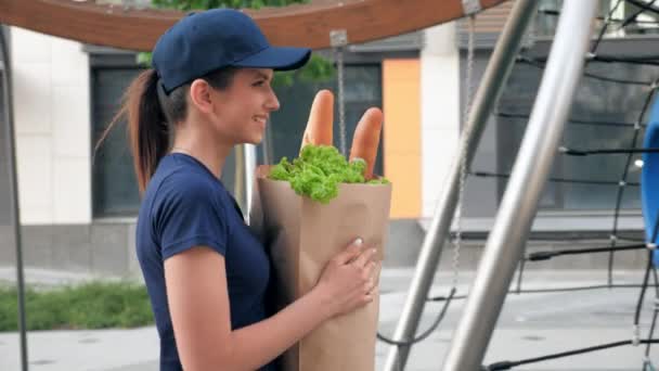 Correio sorridente da mulher da entrega com mantimentos do saco de papel para entregar o cliente da ordem — Vídeo de Stock