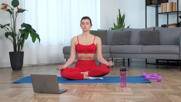 Beautiful fit girl sits meditating in lotus position on sport fitness blue mat — Stock Video