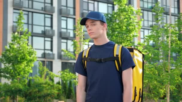 Retrato hombre mensajero entrega de alimentos con mochila térmica gira cabeza mira cámara — Vídeos de Stock