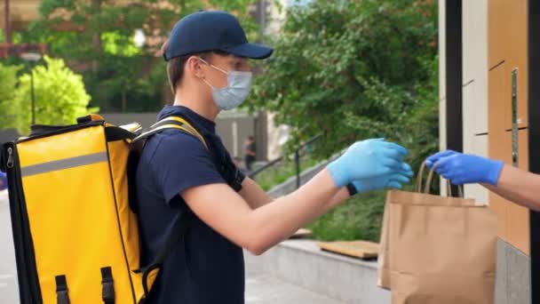 Liefermann trägt medizinische Mundschutz und Handschuhe nimmt Papiertüte entgegen — Stockvideo