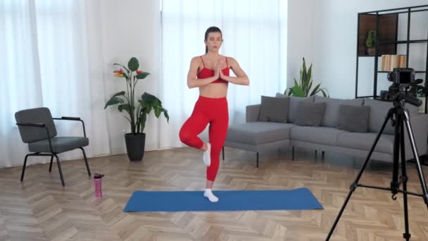 Blogger entrenadora de fitness mujer Fit medita mientras está de pie en la esterilla de yoga en casa — Vídeos de Stock