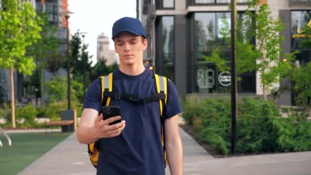 Matleverans man kurir promenader gatan titta på navigering i smartphone — Stockvideo