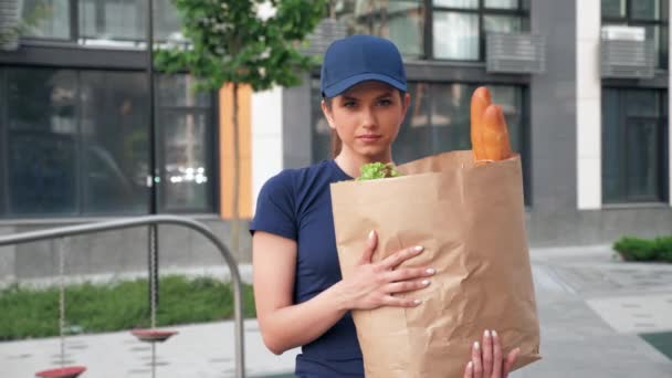 Portrait food delivery mensajero mujer sostiene bolsa de papel con comestibles en las manos — Vídeo de stock