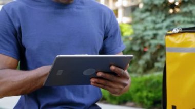 Afro-Amerikan kurye tezgahta otururken tablet kullanıyor.