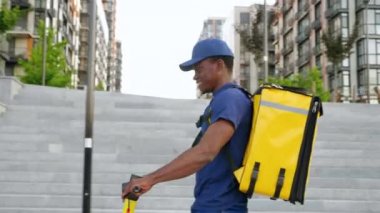Sırt çantalı Afro-Amerikan kurye teslimatı sokak elektrikli scooter 'ı kullanıyor.