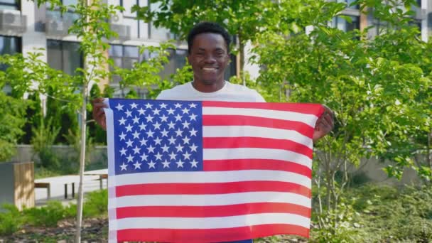 Portrait souriant afro-américain tenant un drapeau américain et regarde la caméra — Video