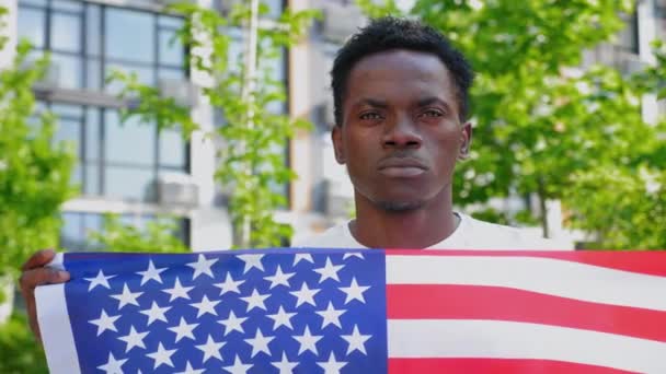 Gros plan homme afro-américain tenant un drapeau américain et regarde la caméra — Video