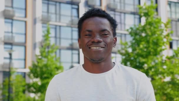 Närbild ler afro-amerikansk man ser kamera på bakgrund modern byggnad — Stockvideo