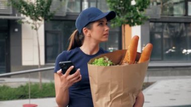 Yemek teslimatçısı kadın kurye akıllı telefon, kağıt torba görünümlü adres kullanıyor.