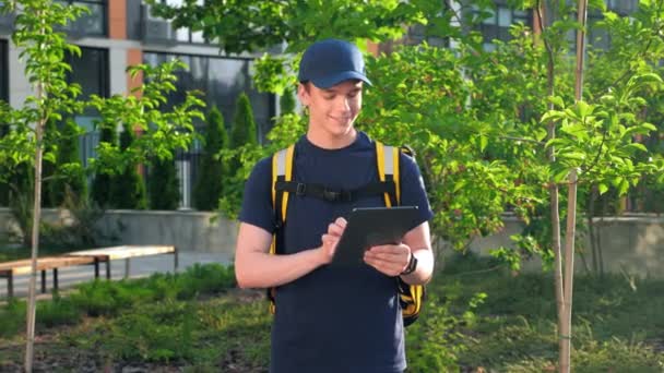 Zoom w uśmiechnięty człowiek kurier dostawy żywności z plecakiem termicznym używa tabletu — Wideo stockowe