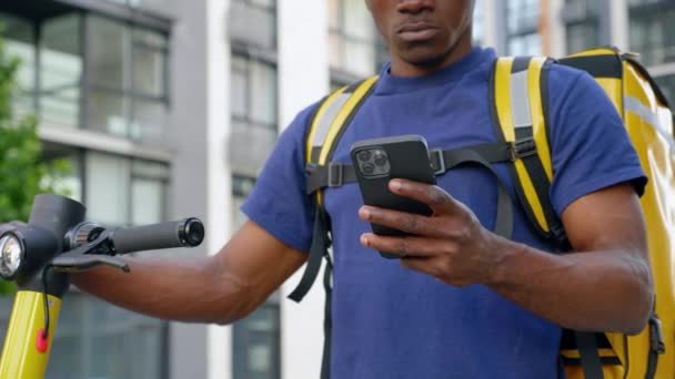Hombre afroamericano mensajero entrega de alimentos con scooter eléctrico utiliza teléfono inteligente — Vídeos de Stock