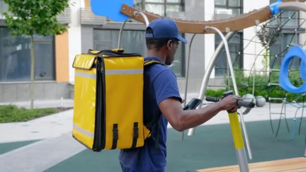 Hombre afroamericano mensajero camina con scooter eléctrico utiliza navegador de teléfonos inteligentes — Vídeos de Stock