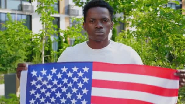 Zoom fotocamera in afro-americano uomo in possesso di una bandiera americana e guarda la fotocamera — Video Stock
