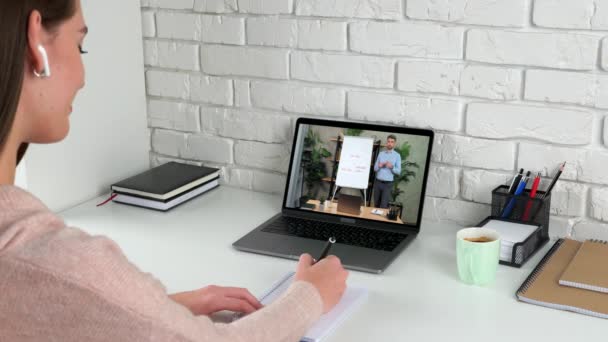 Zakenvrouw op kantoor schrijft in notebook luisteren online video oproep laptop — Stockvideo