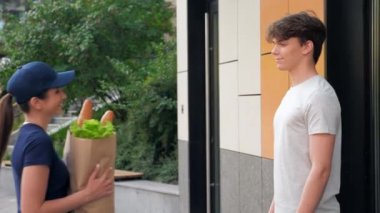 Kadın çalışan teslimatçı mutlu müşteriye market sepeti getiriyor.