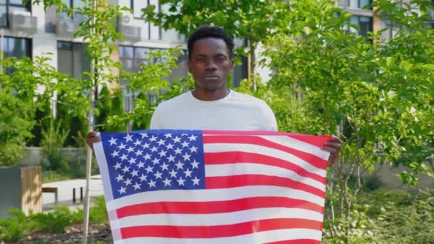 Portret van een Afro-Amerikaanse man met een Amerikaanse vlag en kijkt camera in de zomer — Stockvideo