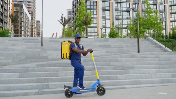 Zoom em correio homem afro-americano de pé com mochila e scooter elétrico — Vídeo de Stock