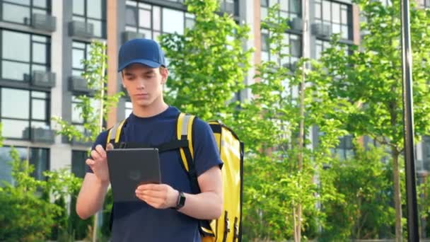 Portrait jovem mensageiro entrega de alimentos com mochila térmica usa tablet — Vídeo de Stock