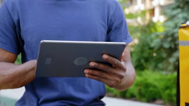 Close up afro-americano homem correio entrega de alimentos sentado no banco usa tablet — Vídeo de Stock