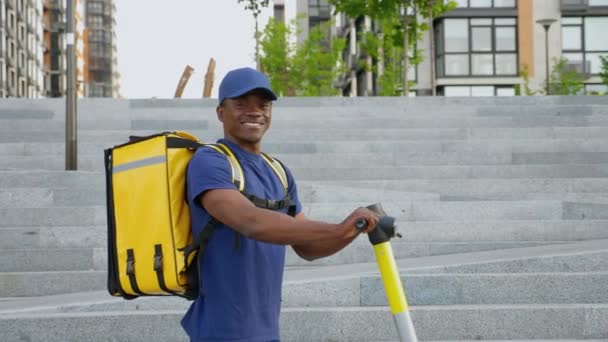 Retrato sonriente afro-americano mensajero hombre con mochila y scooter eléctrico — Vídeos de Stock