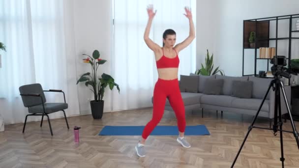 Fit gyönyörű nő fitness edző blogger csinál torna ugrás, edzés otthon — Stock videók