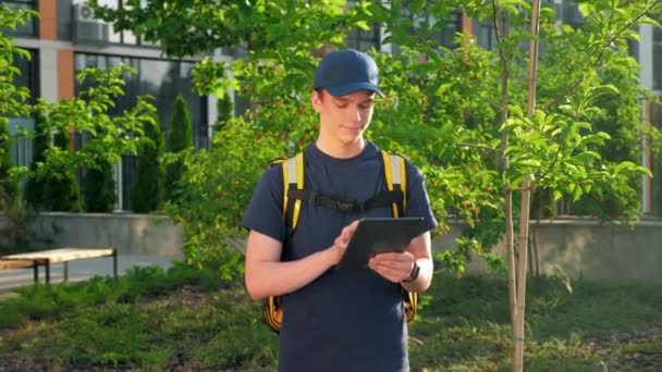 Zoom na entrega de alimentos sorridente mensageiro homem com mochila térmica usa tablet — Vídeo de Stock