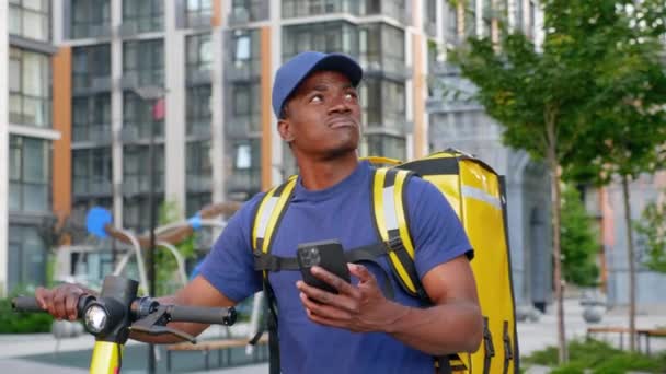 Афро-американец курьер гуляет с электрическим скутером использует смартфон навигации — стоковое видео