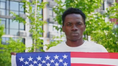 Amerikan bayrağını tutan Afro-Amerikan adam kameraya bakıyor.