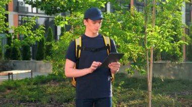 Genç adam kurye yiyecek dağıtımına termal sırt çantalı kamera yakınlaştırması tablet kullanıyor