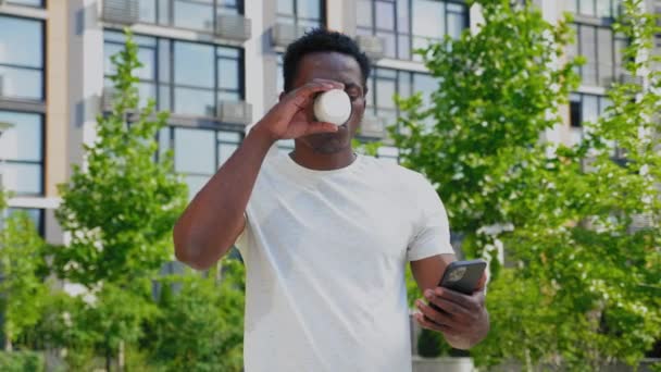ポートレートアフリカ系アメリカ人の男性のフリーランサーは夏にスマートフォン飲料コーヒーを使用しています — ストック動画