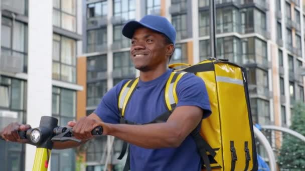 Sonriente hombre afro-americano mensajero entrega camina calle con scooter eléctrico — Vídeos de Stock