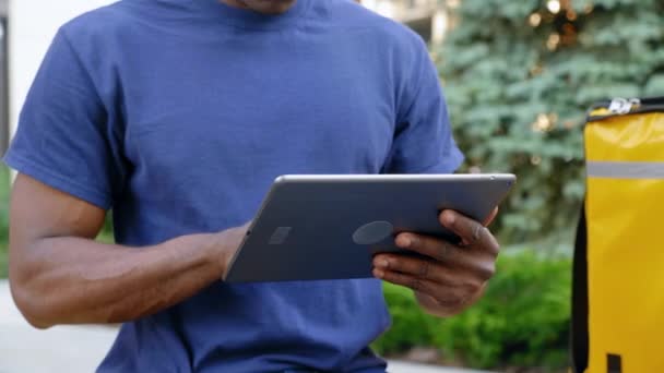 Close up afro-americano homem correio entrega de alimentos sentado no banco usa tablet — Vídeo de Stock