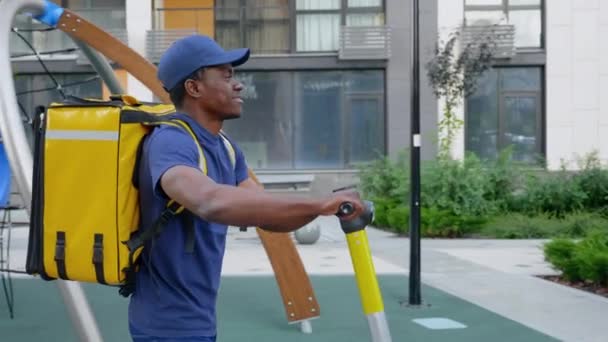 Sonriente hombre afro-americano mensajero entrega camina calle con scooter eléctrico — Vídeos de Stock