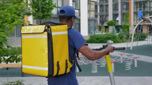 Hombre afroamericano mensajero camina con scooter eléctrico utiliza navegador de teléfonos inteligentes — Vídeos de Stock