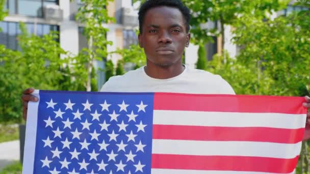 Camera zoom in afro-Amerikaanse man met een Amerikaanse vlag en kijkt camera — Stockvideo