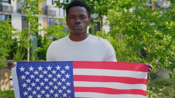 Porträtt afro-amerikan man håller en amerikansk flagga och ser kameran på sommaren — Stockvideo