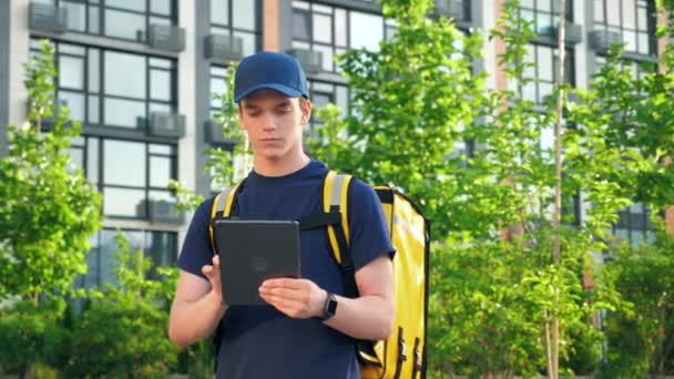 Portrait delivery man courier with thermal backpack uses tablet confirm order — 비디오