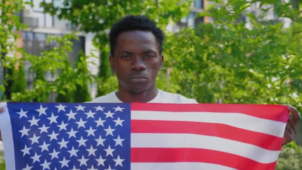 Close up afro-amerikaanse man met een Amerikaanse vlag en ziet er camera in de zomer — Stockvideo