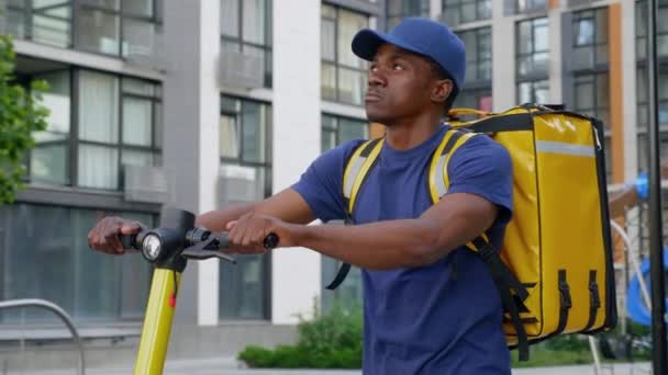 Fiducioso afro-americano consegna corriere cammina strada con scooter elettrico — Video Stock