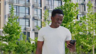Gülümseyen Afro-Amerikalı adam yazın kahve içerken akıllı telefon kullanıyor.