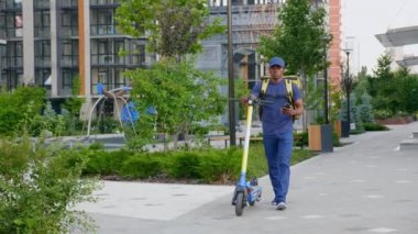 Afro-Amerikan erkek kurye elektrikli scooterla yürüyor akıllı telefon navigasyonu kullanıyor