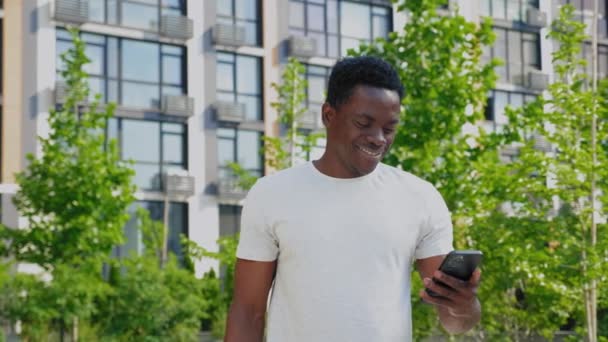 ポートレート笑顔アフロアメリカ人男性は夏にスマートフォン飲料コーヒーを使用しています — ストック動画