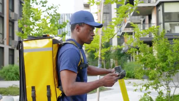 Homem afro-americano mensageiro caminha com scooter elétrico usa smartphone navegar — Vídeo de Stock