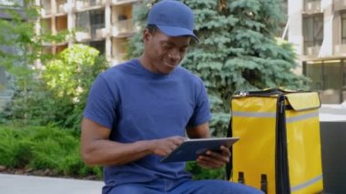 Kürsüde oturan gülümseyen Afro-Amerikan kurye tablet görünümlü kamera kullanıyor.