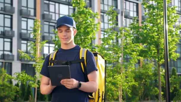 Retrato hombre sonriente mensajero entrega de alimentos con mochila térmica utiliza tableta — Vídeos de Stock