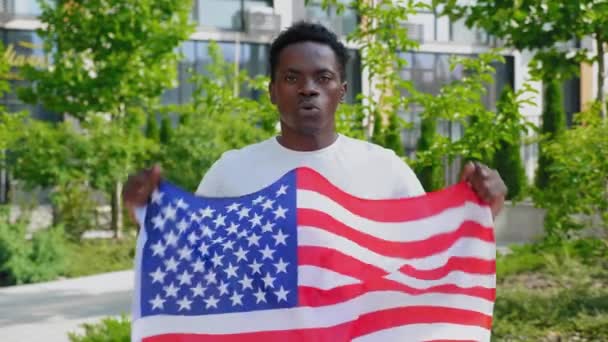 Portret van een Afro-Amerikaanse man met een Amerikaanse vlag, kijkt camera en zegt USA — Stockvideo