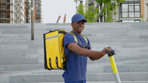 Portrait homme afro-américain souriant courrier avec sac à dos et scooter électrique — Video