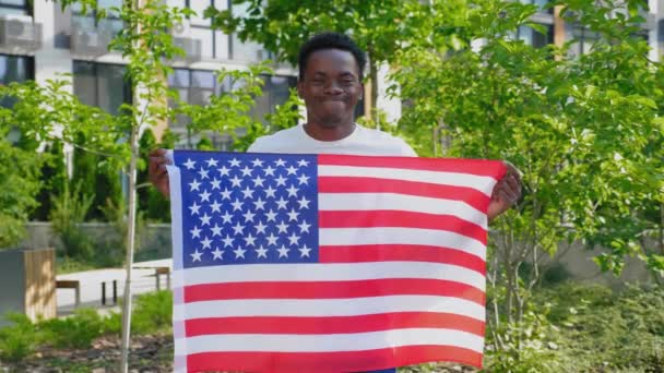 Portrait souriant afro-américain tenant un drapeau américain et regarde la caméra — Video