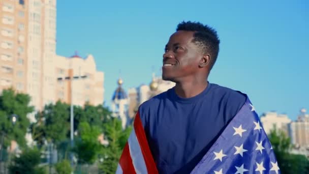 Sonriente hombre afroamericano caminando por la calle con bandera americana en verano — Vídeos de Stock