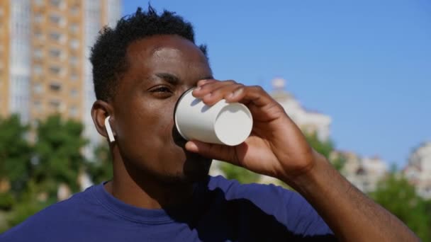 Afrika kökenli Amerikalı serbest çalışan, kablosuz kulaklık takan adam kahve içiyor. — Stok video